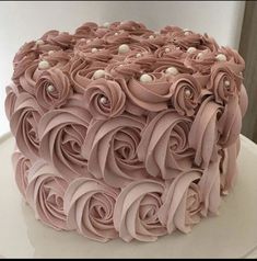 a cake with pink frosting and rosettes on top is sitting on a white plate