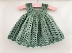 a green crocheted dress hanging on a pink hanger next to a white wall