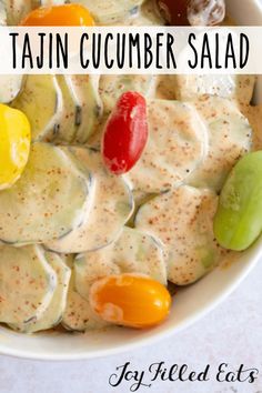 a white bowl filled with tasty cucumber salad next to an orange and green pepper