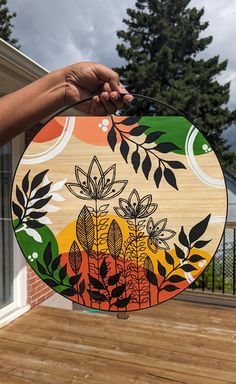 a person holding up a wooden board with flowers and leaves painted on the front side