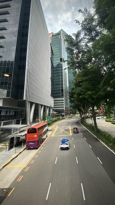 two cars are driving down the road in front of tall buildings and trees on both sides