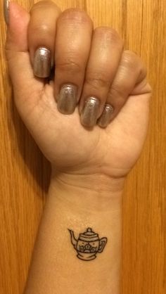 a woman's wrist with a small teapot tattoo on the left side of her arm