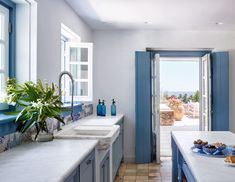 a kitchen with blue and white cabinets, counter tops, and sink in front of an open door