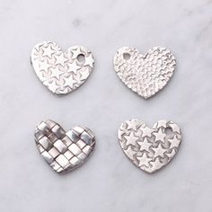 four silver heart shaped charms on a marble surface, one has a basket weave design and the other has a star pattern