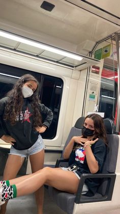 two women wearing face masks sitting on a subway train, one with her legs crossed