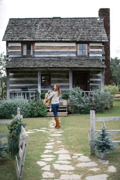 a woman standing in front of a wooden house with a stone path leading to it