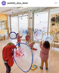 three children are playing with plastic discs in a room that is decorated with windows and wood flooring