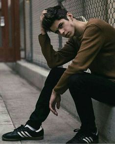 a young man sitting on the side of a building leaning against a fence with his hand on his head