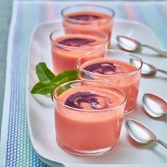 three glasses filled with fruit and garnished with mint on a white plate next to spoons