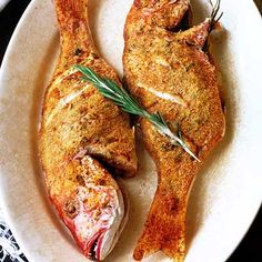 two pieces of meat on a white plate with green garnish and rosemary sprigs