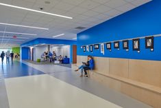 a woman sitting on a bench in a blue and white hallway with people walking by