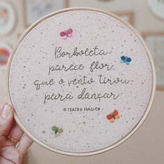 a person holding up a cross - stitch quote in front of a wall with butterflies on it