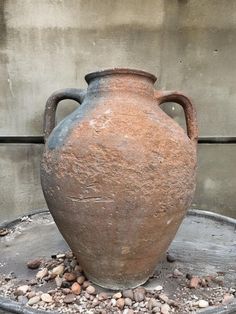 an old clay vase sitting on top of a metal tray filled with rocks and gravel