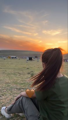 a woman sitting on the ground with her hair blowing in the wind at sunset or dawn