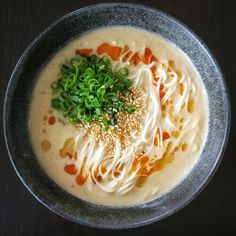 a bowl of soup with noodles, carrots and green garnish on top