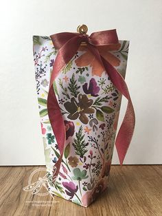 a gift bag with a red ribbon tied around it on a wooden table next to a white wall