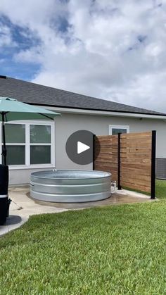 an outdoor hot tub sitting in the middle of a yard next to a fence and umbrella