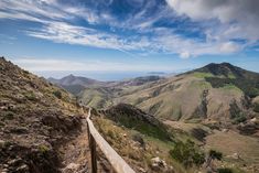 a wooden walkway on the side of a mountain with mountains in the background and blue sky