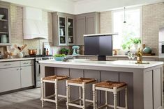 a kitchen with grey cabinets and white counter tops, two stools in front of the island