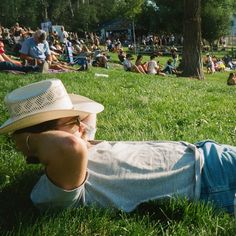 a man laying on the grass with his head in his hands while wearing a hat