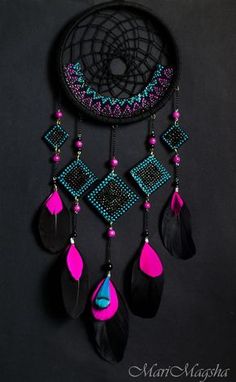 a black and pink dream catcher with feathers hanging from it's side on a dark background