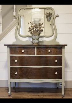 an old dresser with flowers in a vase on top and a mirror over the top