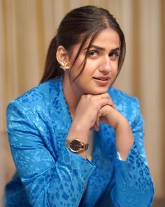 a woman sitting down with her hand on her chin and looking at the camera while wearing a blue jacket