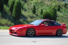 a red sports car driving down the road with trees in the backgrouund