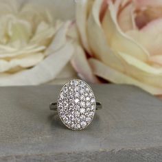 a close up of a ring on a table with flowers in the background and a rose behind it