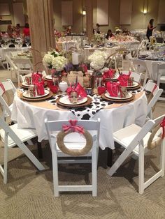 a table set up with white chairs and red bows on the centerpieces for an event