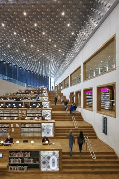 people are walking up and down the stairs in a library with many bookshelves