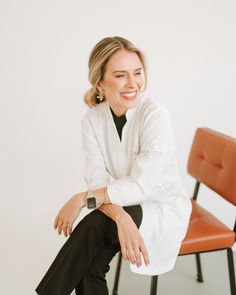 a woman sitting on top of a brown chair next to a red chair and white wall