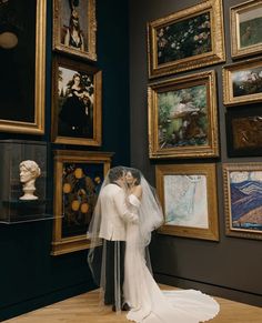 a bride and groom are kissing in front of paintings on display at the art museum