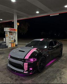 a black car with pink stripes parked at a gas station