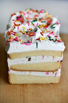 a piece of cake with white frosting and sprinkles on it sitting on a wooden table