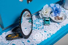 there is a blue dresser with white lace on it and some flowers in the mirror