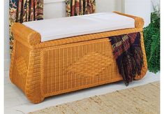 a wicker bench with white cushions in front of a window and curtains behind it