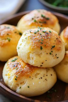 small rolls are piled on top of each other in a wooden bowl with parsley sprinkled on top