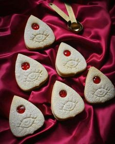 four cookies with red cherries are arranged on a pink satin covered tablecloth, next to a pair of scissors