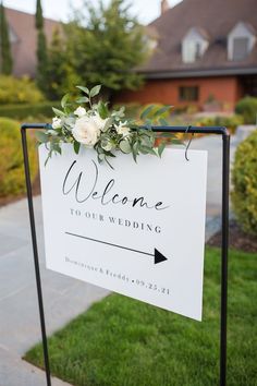 a welcome sign with flowers and greenery on it in front of a large house