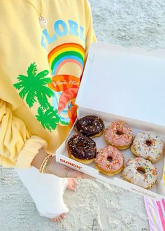 a person holding a box of doughnuts with sprinkles