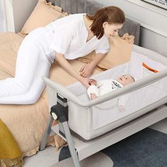 a woman in white shirt laying on bed next to baby in crib with mattress