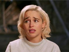 a woman with blonde hair wearing a white sweater looking at the camera and making a surprised face