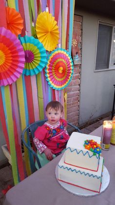 a small child sitting in front of a birthday cake on a table with paper fans