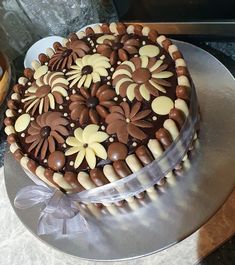 a chocolate cake with white and brown flowers on it sitting on a silver platter