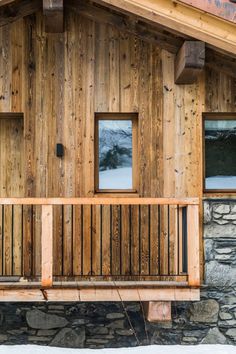 a wooden building with two windows and a bench in front of the window is snow covered ground