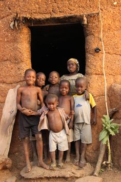 a group of young children standing in front of a mud hut with an open door