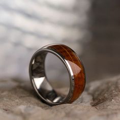 a silver ring with wood inlays on top of a stone surface, resting on a rock