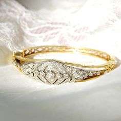 An astounding Edwardian era diamond cluster hinge bangle bracelet in 14k yellow gold and platinum. Features an ornate diamond-encrusted platinum navette setting mounted on a tapered gold band with cutout embellishments and a latch box clasp. Built into the focal point of this bracelet is 5 round-cut diamonds secured in a horizontal line of bezel settings. The open work on either side of the platinum setting is also decorated with three prong-set diamond accents. All the diamonds seem to be in go Vintage Diamond Bracelet With Brilliant Cut For Formal Occasions, Elegant Oval Bangle With Single Cut Diamonds, Vintage White Gold Bracelet With Single Cut Diamonds, Vintage White Gold Bracelets With Single Cut Diamonds, Vintage White Gold Diamond Bracelet With Brilliant Cut, Vintage Diamond Bracelet For Anniversary, Vintage Brilliant Cut Diamond Bracelet For Wedding, Formal Oval Bangle With Diamond Accents, Vintage Diamond Cut Bracelet For Wedding