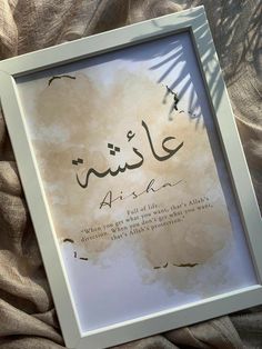 an arabic calligraphy displayed in a white frame on a bed with brown linens